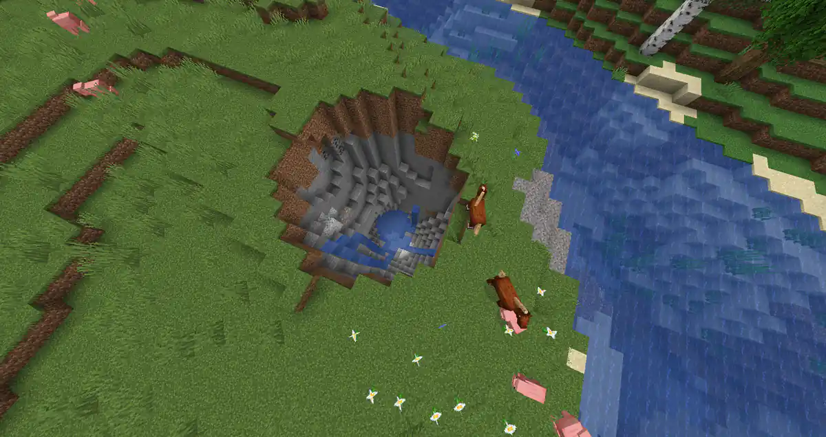 A deep round crater in a grassy field next to a river, with stone and water at the bottom and pigs and horses grazing around the edge