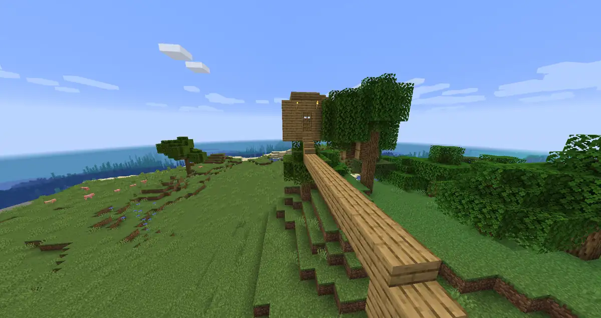 A small wooden tree house built into an oak tree on a grassy hill, reached by a long plank bridge that runs up the slope, with pigs grazing and the sea in the distance