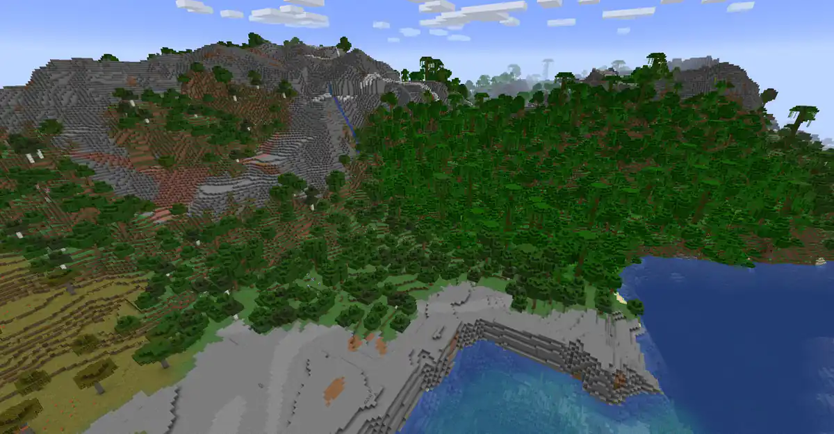 A coastline seen from high above, with grey stone peaks, a waterfall and dense jungle running down to a stony shore and a blue bay