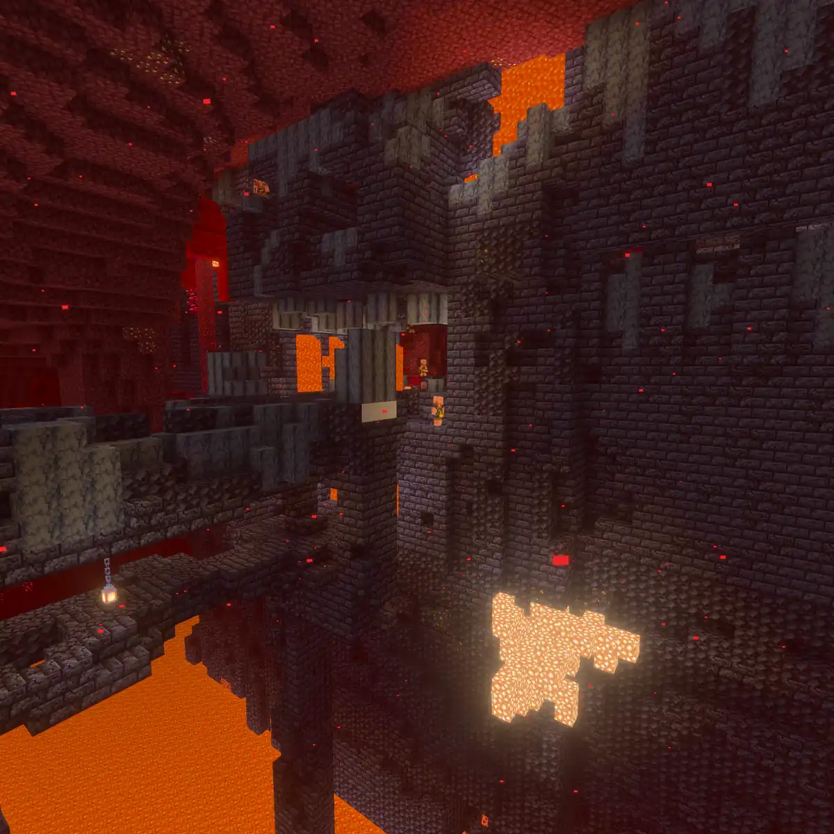A huge ruined fortress of dark blackstone bricks in the Nether, with a crumbling bridge, a glowing patch in its wall and lava far below under a red netherrack ceiling