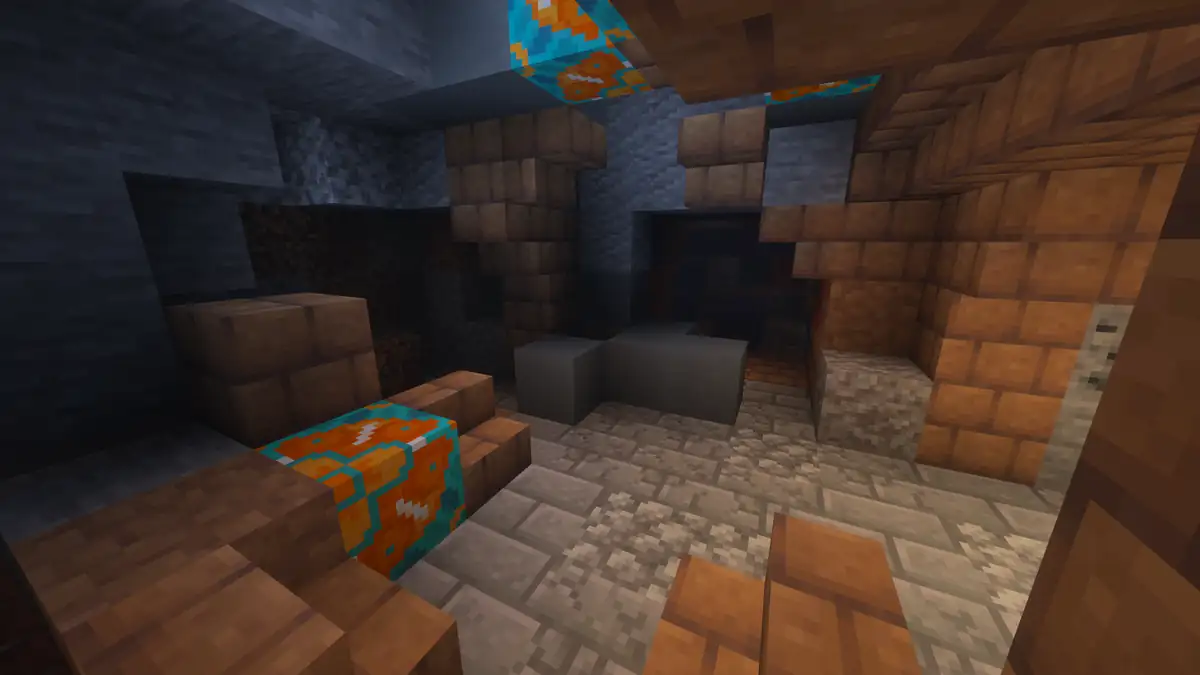 A half buried room of terracotta and mud bricks inside a stone cave, with two blocks of orange and turquoise glazed terracotta, a gravel floor and a dark doorway at the back