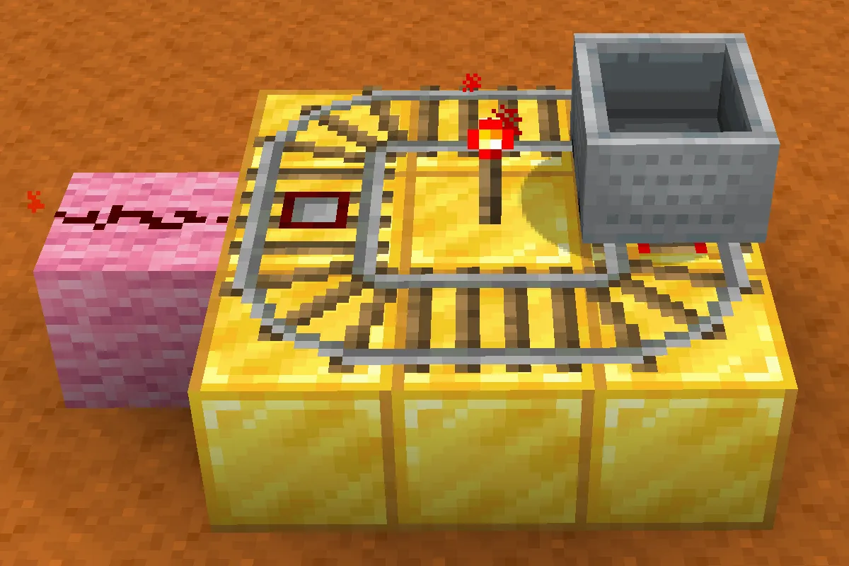 A redstone clock built from a minecart on a small loop of rails on top of gold blocks, with a redstone torch in the middle of the loop and a pink block at the side, on red sand