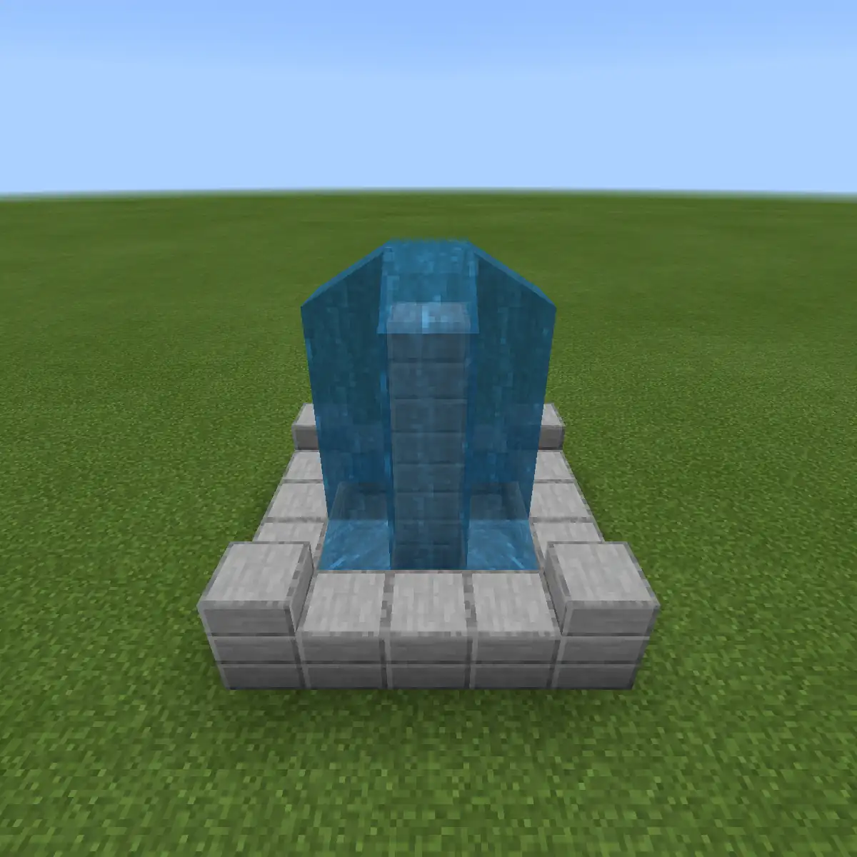 A small Minecraft fountain of stone bricks with a column of water pouring down all four sides into the basin, standing alone on flat grass under a pale blue sky