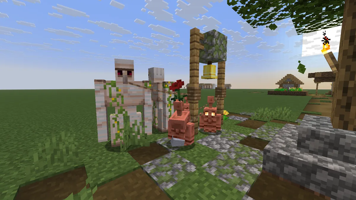 Two iron golems covered in vines and two small copper golems standing on a mossy cobblestone path beside a village bell that hangs from a wooden frame, with a red flower above one of the copper golems